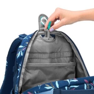 Person’s hand adjusts a teal-tipped clip on the top of a blue floral backpack, revealing gray interior with pockets