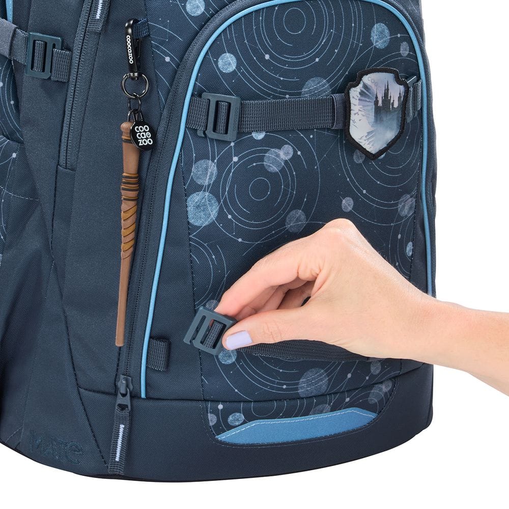 Close-up of a dark blue backpack being fastened with a side strap buckle; space-pattern fabric, zip pulls, and a small crest on the pocket.